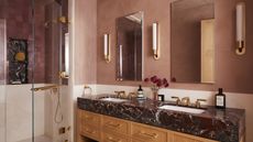 A bathroom with pink walls, a double vanity with a red marble countertop, and a shower with pink zellige tiles