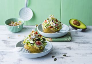 2 jacket potatoes topped with a salad in a bowl on a white sideboard