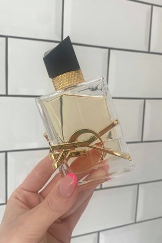 Original image showing hand holding a bottle of YSL Libre perfume against a white tiled background