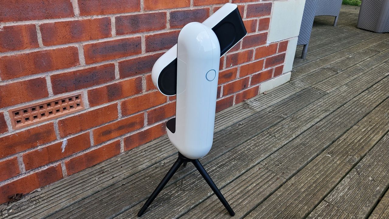 Image of the Vaonis Vespera Observation Station. It's a sleek white capsule balanced on a black tripod. It's facing forward. There is the outline of a blue circle which is a button near the top of the item. The telescope/camera arm is open at the moment, pointing upwards.