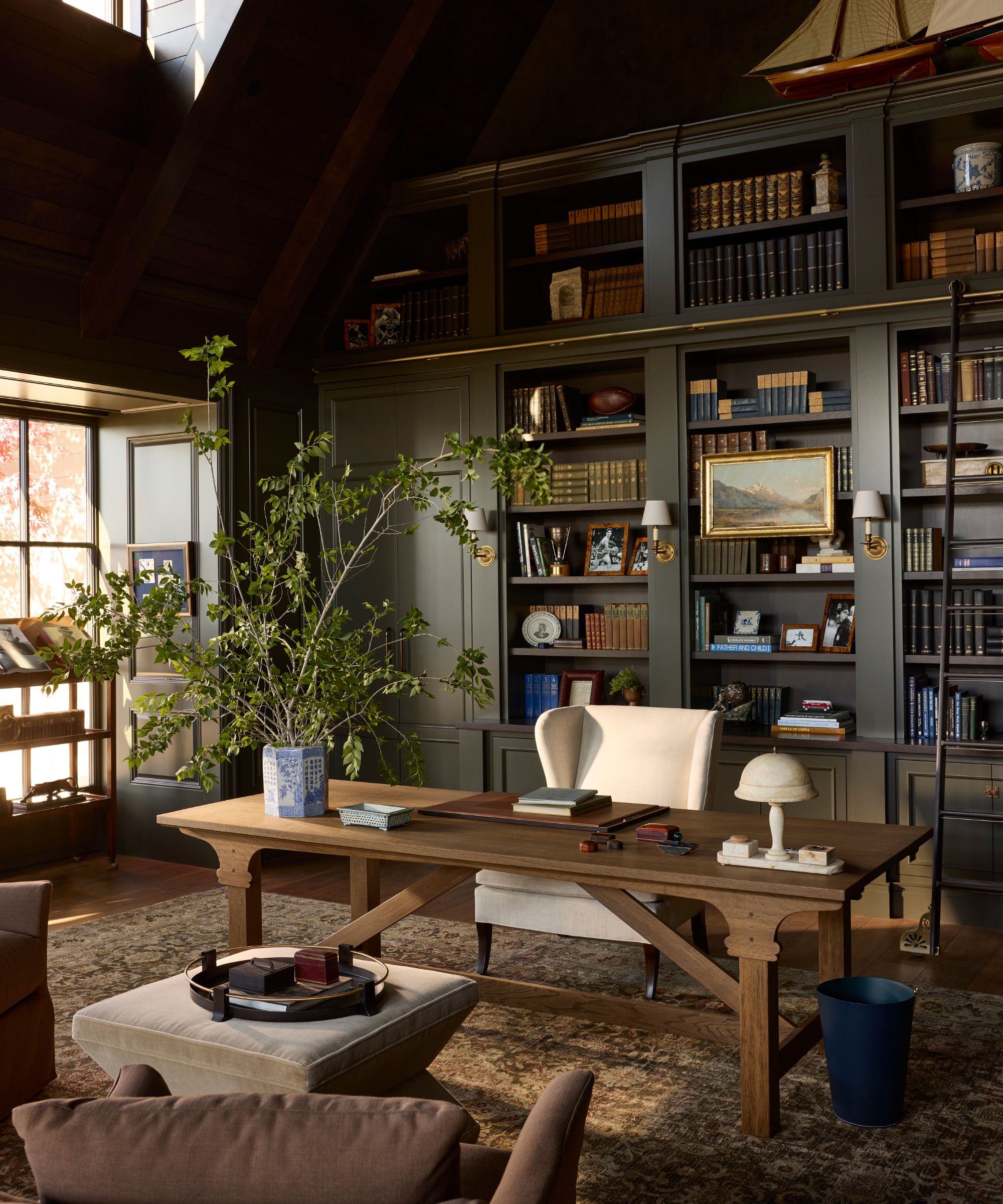 a dark navy home office with library style bookcases and a large wooden desk