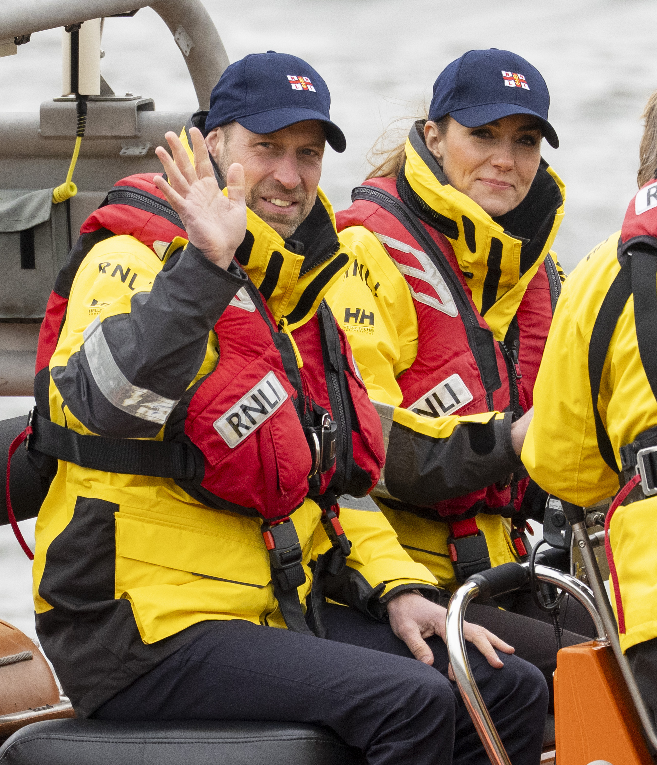 Prince William and Princess Kate wearing life jackets and baseball hats on a boat