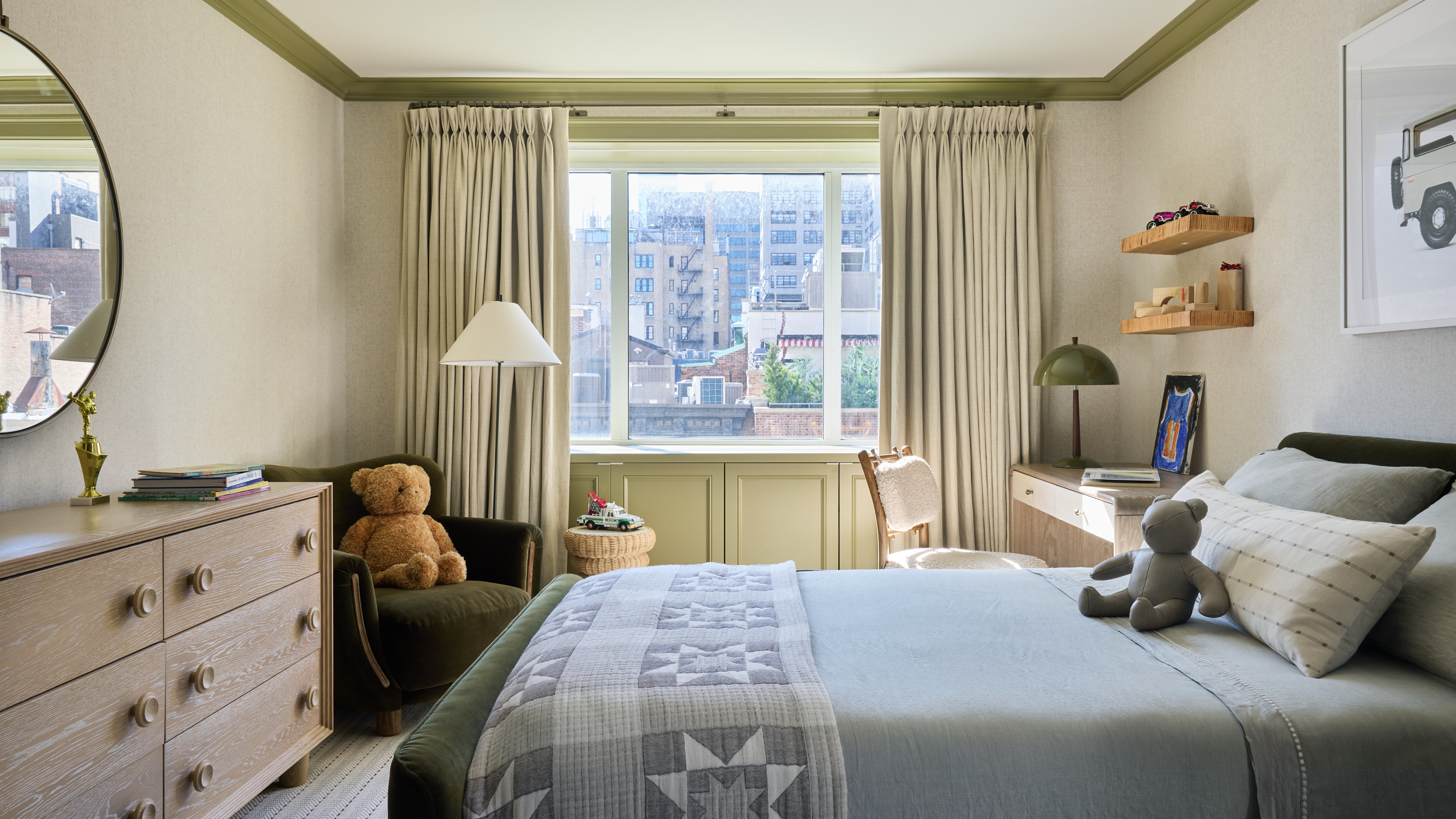 Boy&amp;rsquo;s bedroom with olive velvet bed, green-painted woodwork, neutral wallpaper, timber furniture and an olive desk lamp.