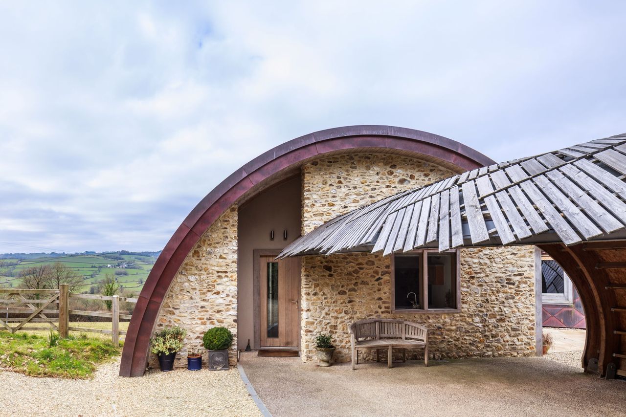 A small side building to the house has timber roofs and stone walls in a dome structure