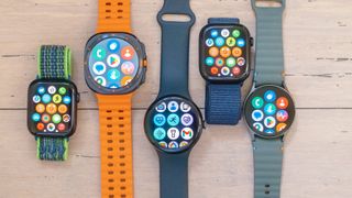 A close-up of five smartwatch on a wooded surface including the Apple Watch SE, Samsung Galaxy Watch Ultra, Google Pixel Watch 3 XL, Apple Watch 10 and Samsung Galaxy Watch 7