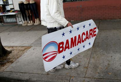 A man holds a sign directing people to sign up for Obamacare. 