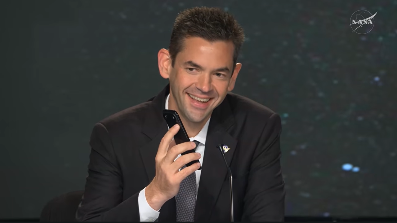 Jared Isaacman holds a cell phone near a microphone.
