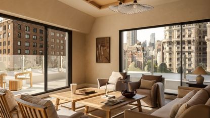 A neutral living room in a penthouse with a balcony running around it with a glass balustrade with two matching wood coffee tables in the center of mirroring armchairs and a sofa