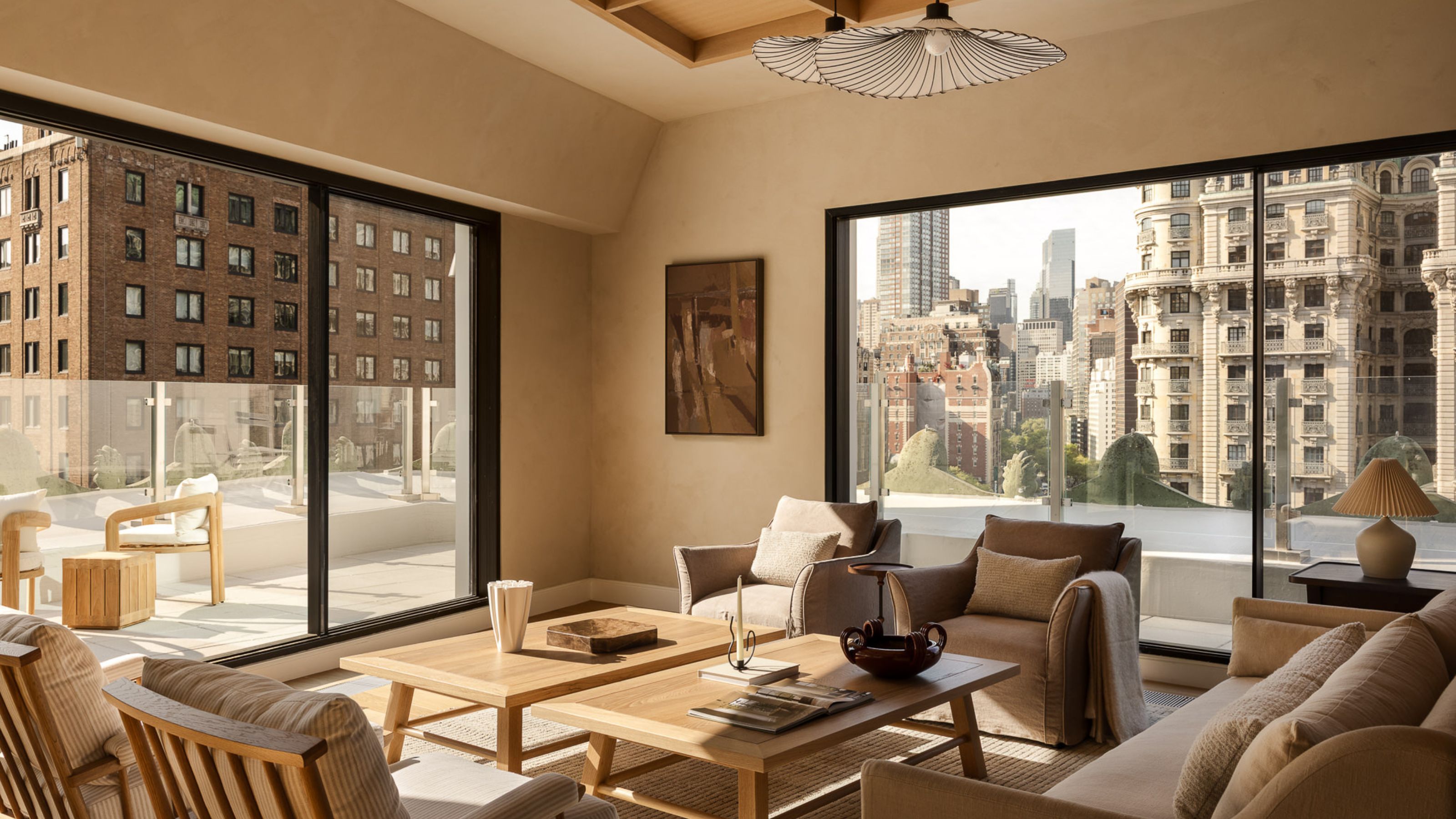 A neutral living room in a penthouse with a balcony running around it with a glass balustrade with two matching wood coffee tables in the center of mirroring armchairs and a sofa