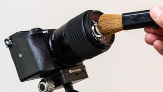 A hand using a brush to clean a camera lens
