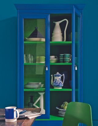 A blue kitchen cabinet with green flocked shelves, assorted ceramic and glass tableware