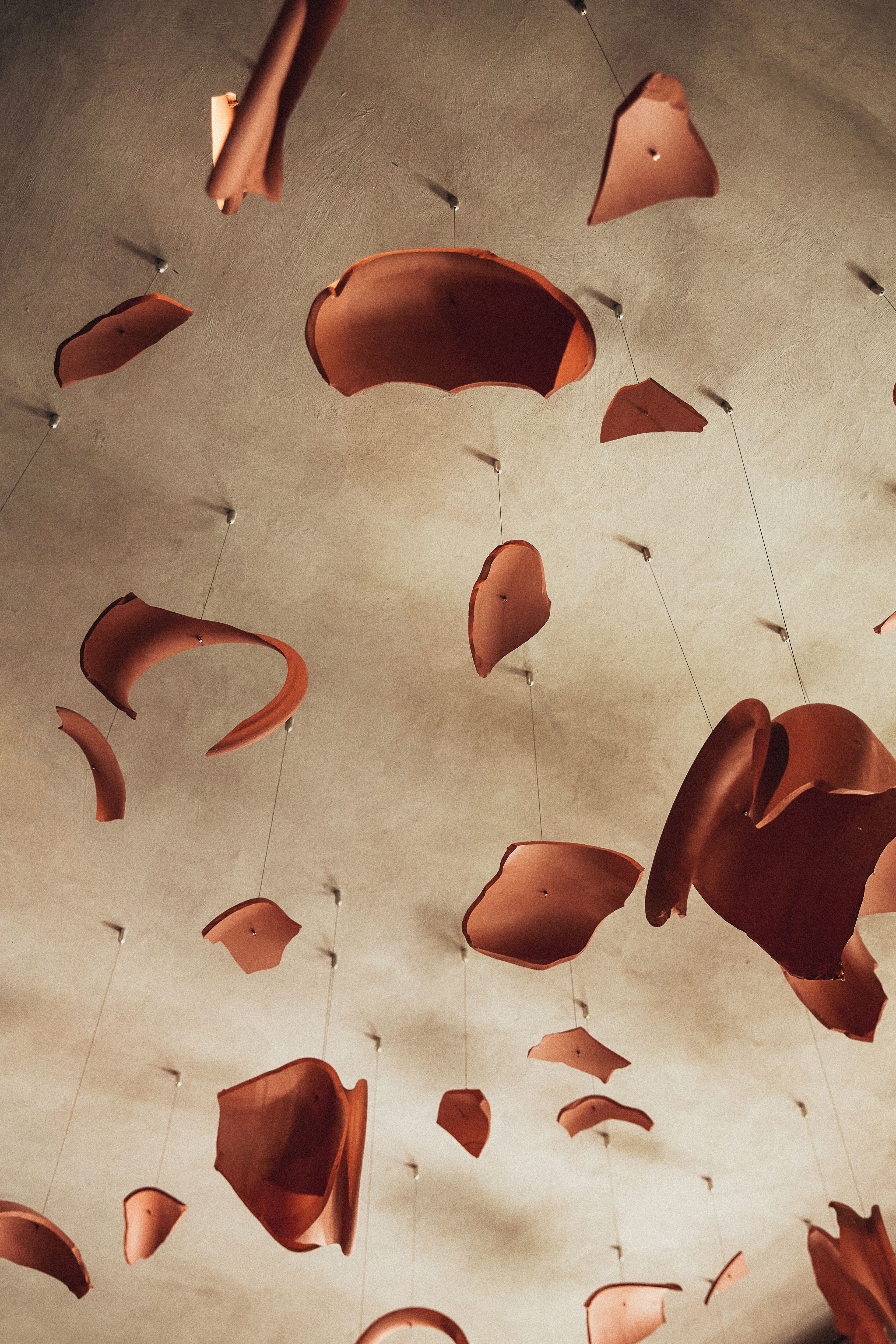 A beige-painted plaster ceiling covered in pendant ceramic sculptures in terracotta hue.