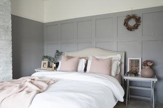 Bedroom with light grey wall panelling, cream bed, white and pink bedding and a white painted brick fireplace