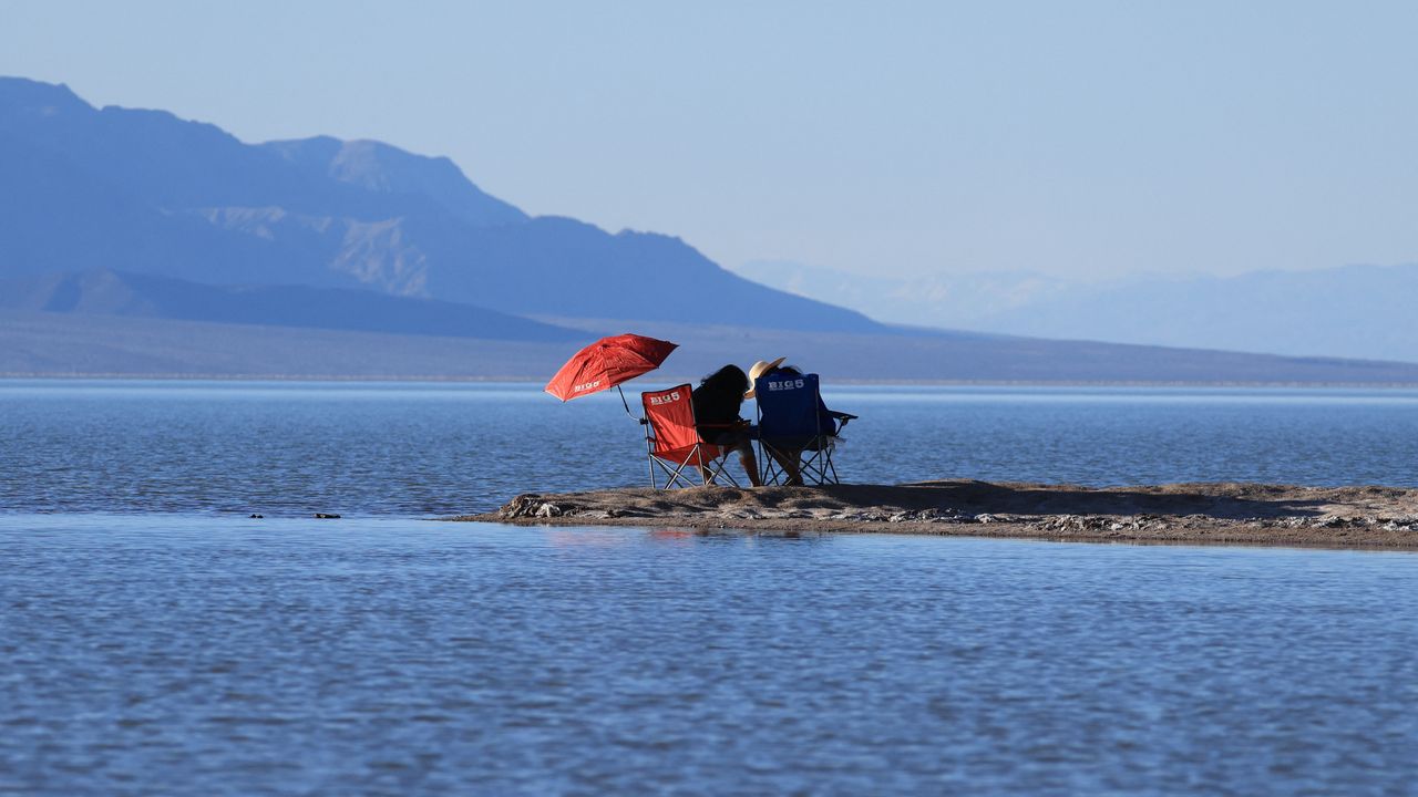 People relax by the water's edge as they enjoy the rare opportunity to see water during their visit to Badwater Basin, the normally driest place in the US,