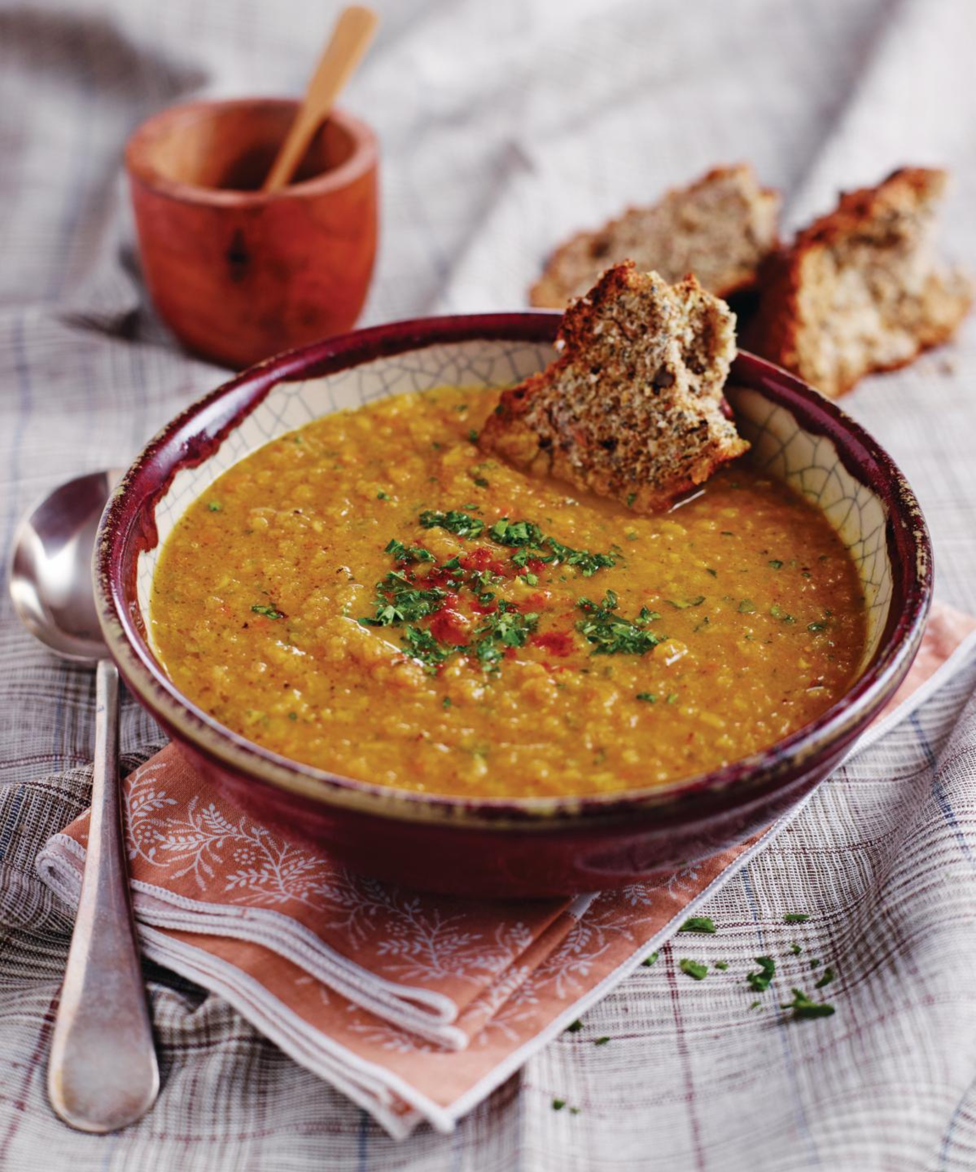 A spiced lentil soup served in a rustic bowl, with crusty wholemeal bread