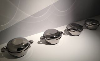 White wall and floor, line of four stainless steel muscle pots with lids