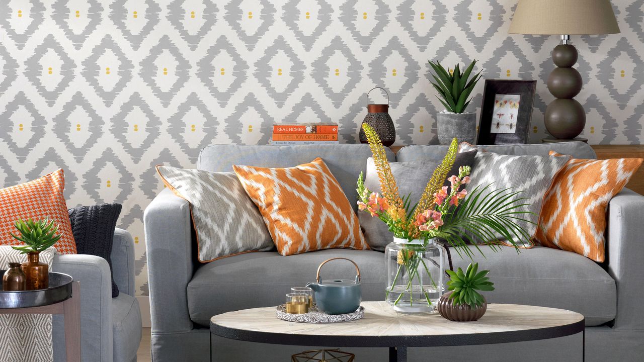 Living room with grey geo wallpaper wall in front of a grey sofa with orange accent cushions