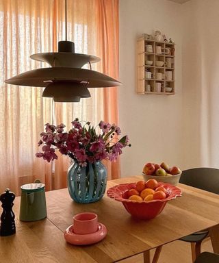 A dining table with colorful dinnerware and bowls, flowers, and a pendant light over it