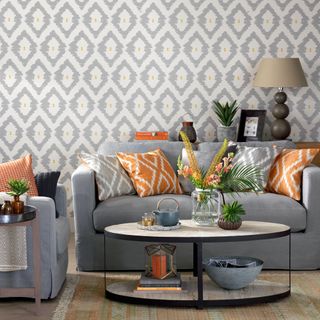 Grey living room with geometric wallpaper, grey sofas and orange accents