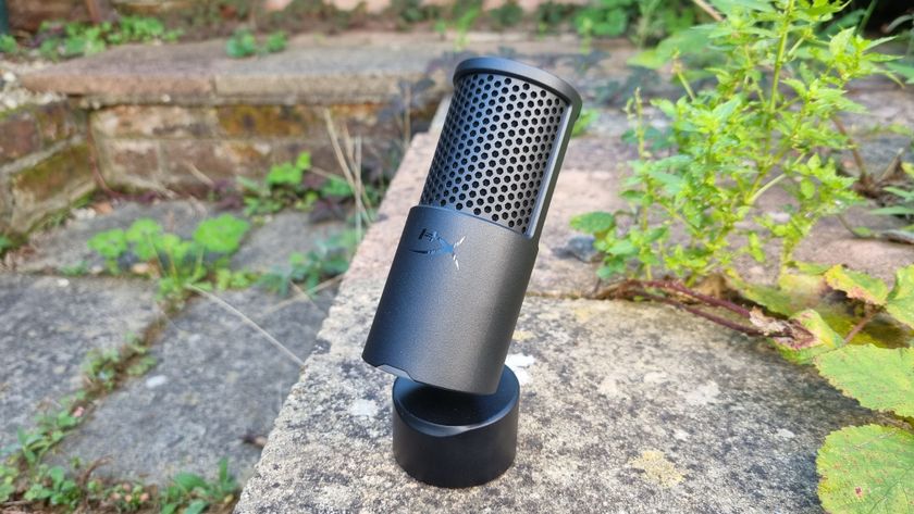 The HyperX SoloCast 2 USB microphone outside amid some foliage, with its base tilted