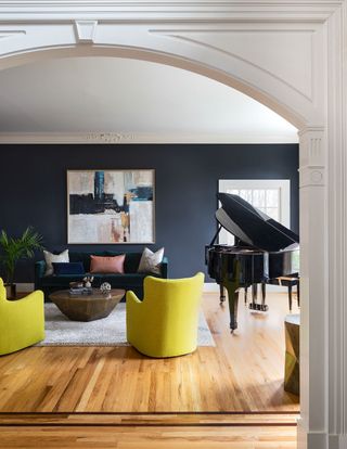 Living room with blue walls, two yellow accent chairs, black piano, green velvet sofa with large abstract artwork above