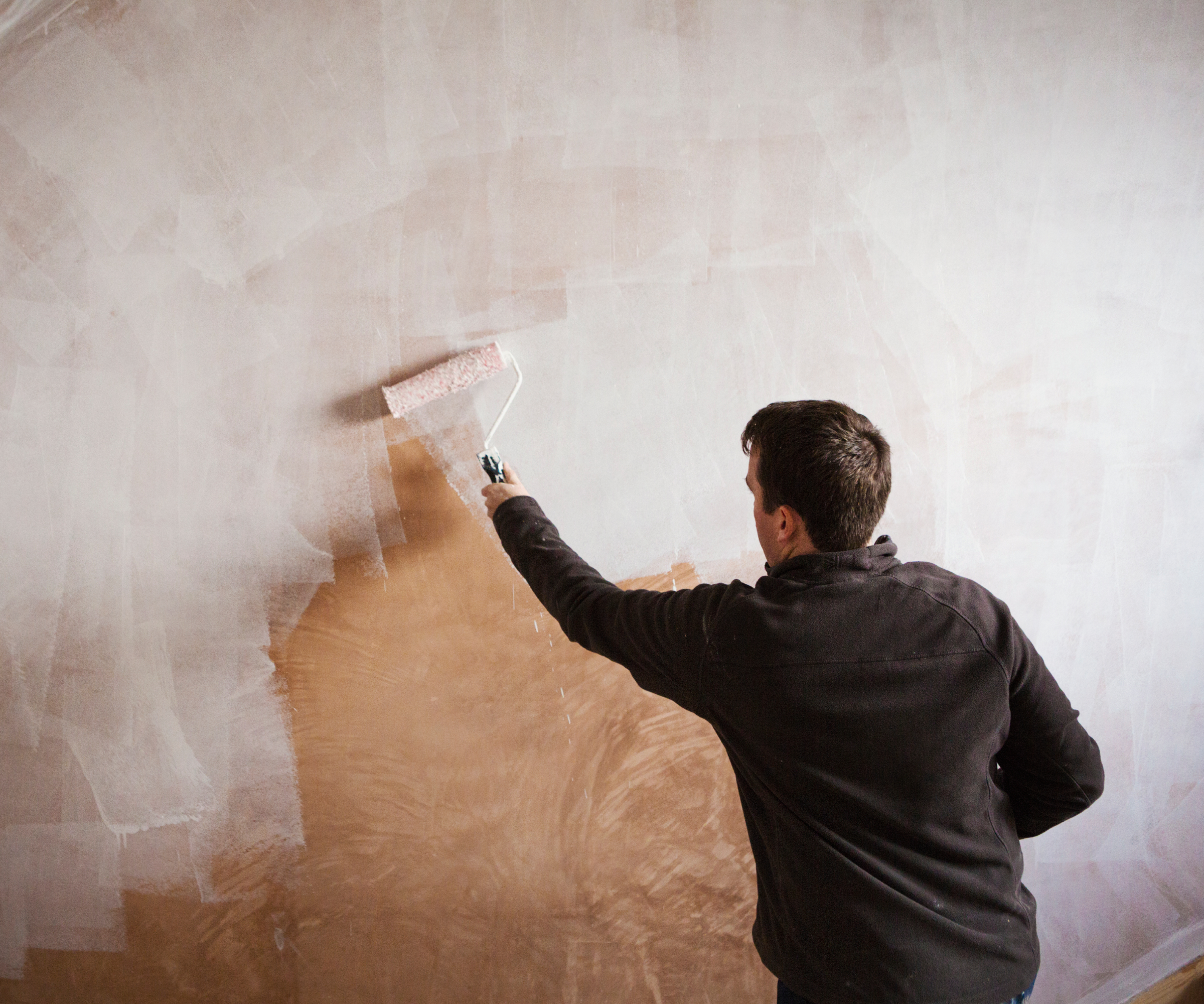 man using roller to cover walls with white paint