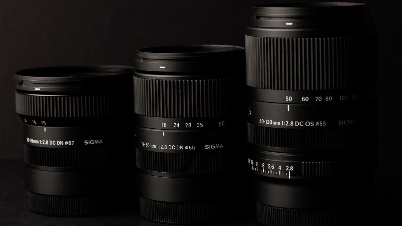 Sigma 50-120mm F2.8 DC OS Contemporary lens alongside two other f/2.8 zoom lenses, in a lowkey lit studio with dark background