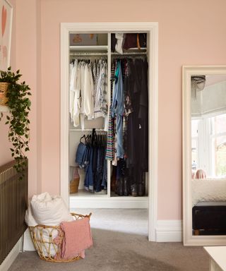 A walk-in wardrobe in bedroom painted pink with large full length mirror