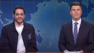 Pete Davidson and Colin Jost sit at the Weekend Update table telling jokes.