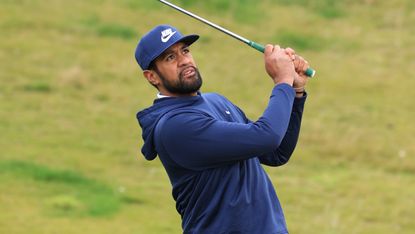 Tony Finau wearing a navy hoodie and cap while holding his finish on a wedge shot