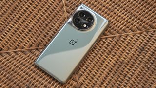 OnePlus 11 i grønt på en flettet kurv med skjermen vendt ned.