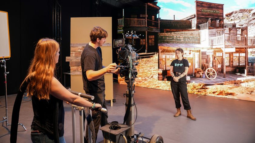 A close-up view of three people working around a camera rig on a dolly in a film studio, with the LED screen backdrop showing the Wild West town.