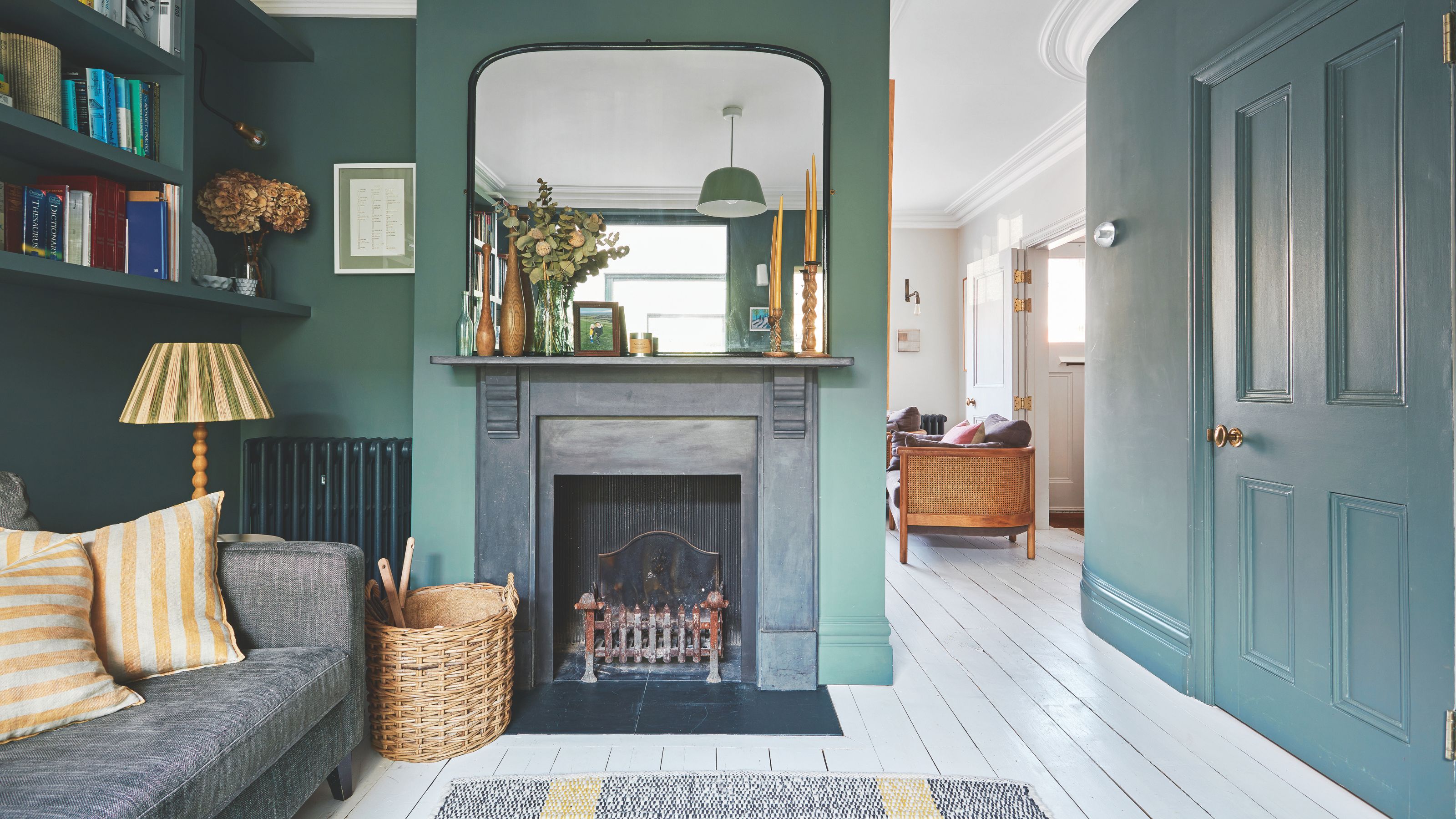 Green painted living room with white wooden floors, a grey sofa on the left and a fireplace in the middle