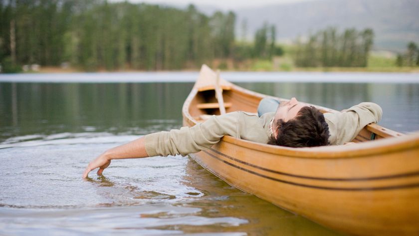 A man lying with his eyes closed in a canoe on a lake, a visualization used in the Military Sleep Method.