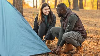 Man and woman pitching a tent in the woods