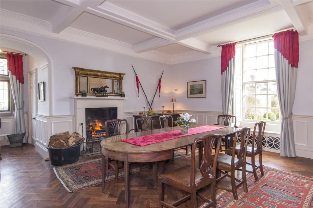 A large dining table inside a dining room with open fireplace and red table cloth