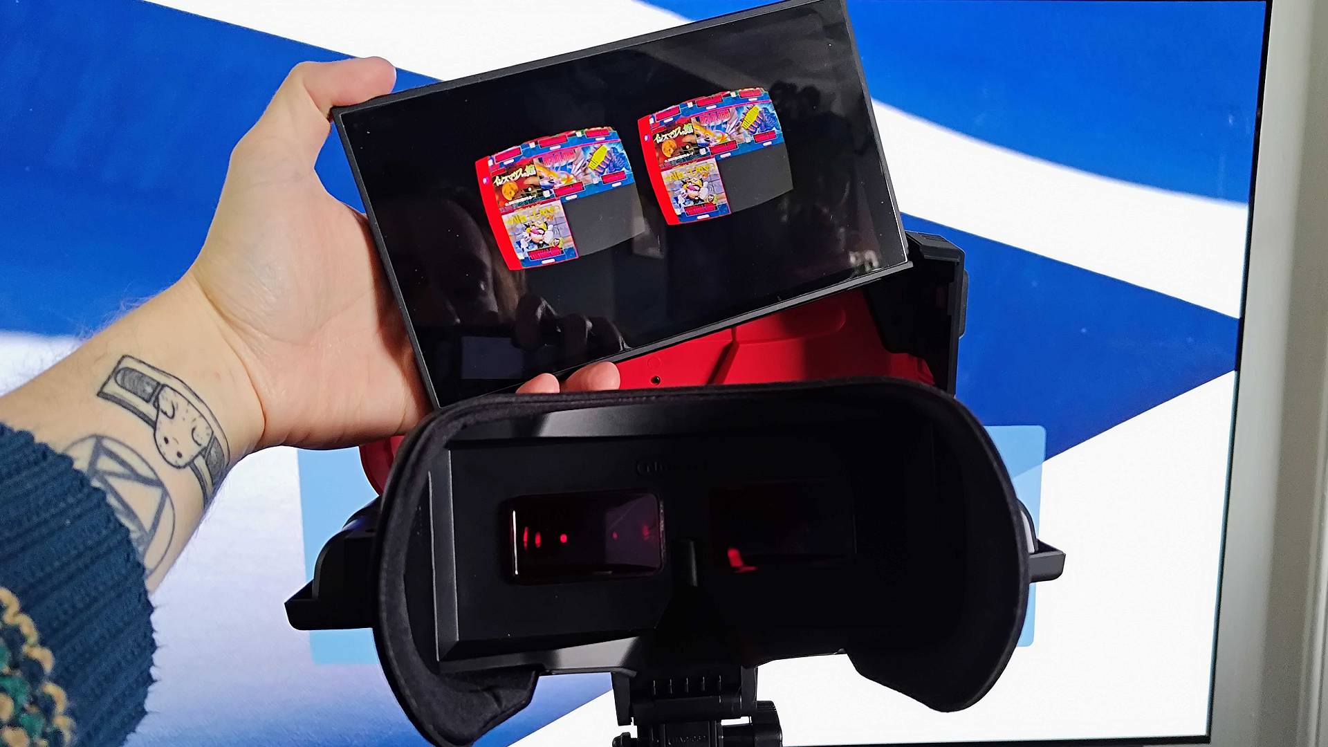 Hand holding Switch 2 next to Virtual Boy with stereoscopic visuals of Switch Online library on screen.