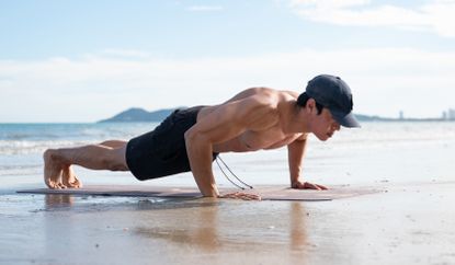 Asian man doing push ups on the beach