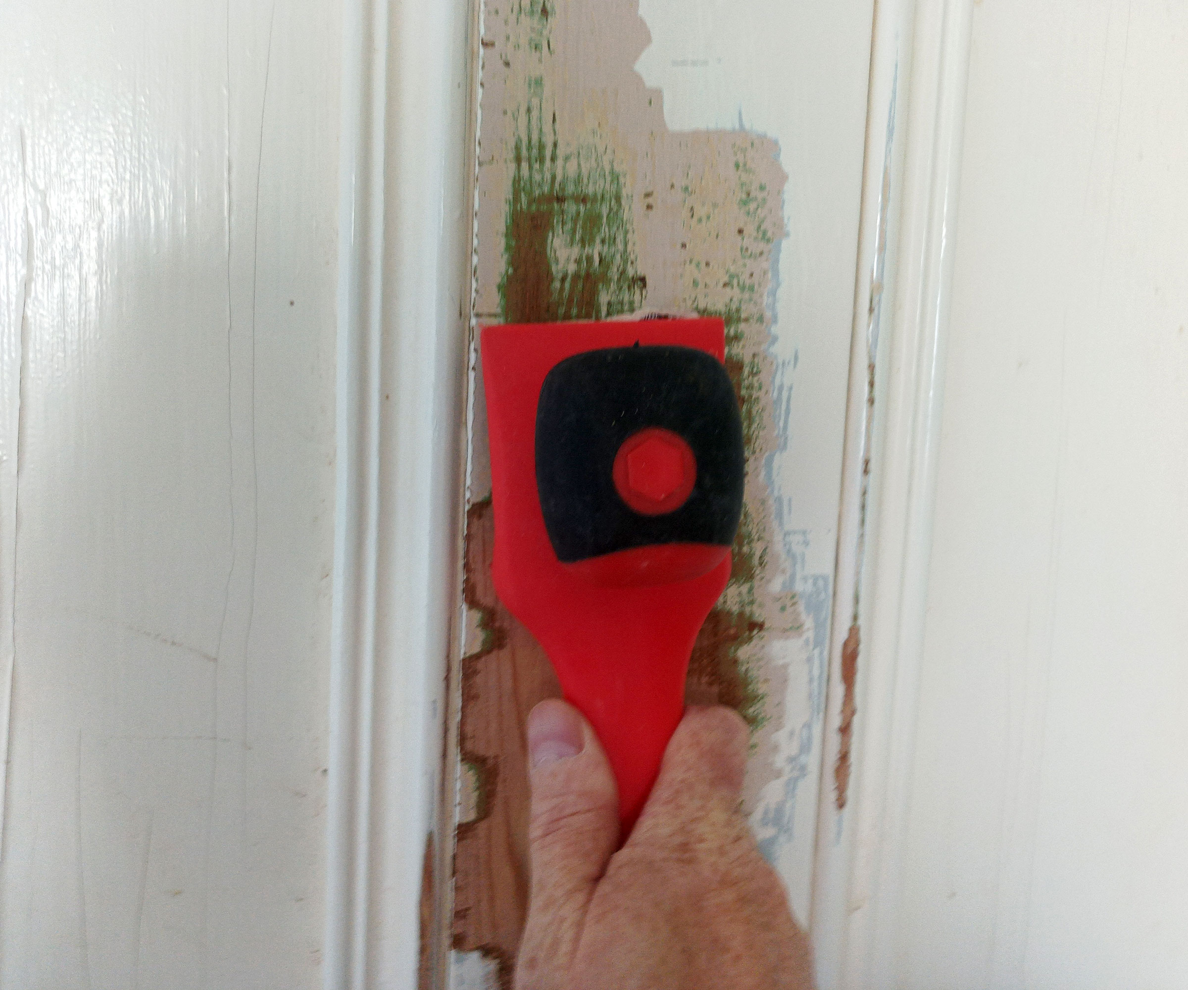 Red heavy duty paint scraper removing old white paint from a panel door
