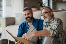Two men with beards, one older and one younger, sit together and look at a photo album.