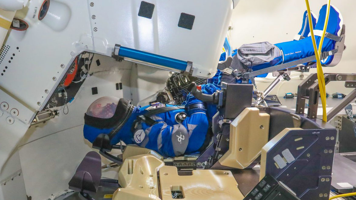 mannequin wearing a spacesuit lies in a spacecraft seat legs up