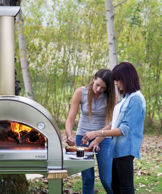 two women preparing pizza next to a wood-fired pizza oven