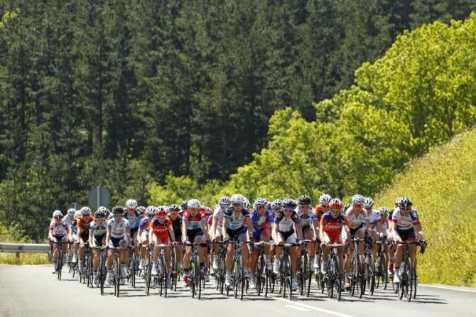 Dwarfed by the mountainous backdrop, the peloton climbing in the sun