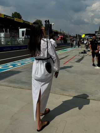 Kelly Piquet wearing a white dress, lat sandals, and an Alaïa heart bag in Monza, Italy at the Italian Grand Prix.