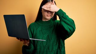 Nuori aasialainen nainen kädet silmien edessä vihreässä neuleessa kannettava tietokone kädessä