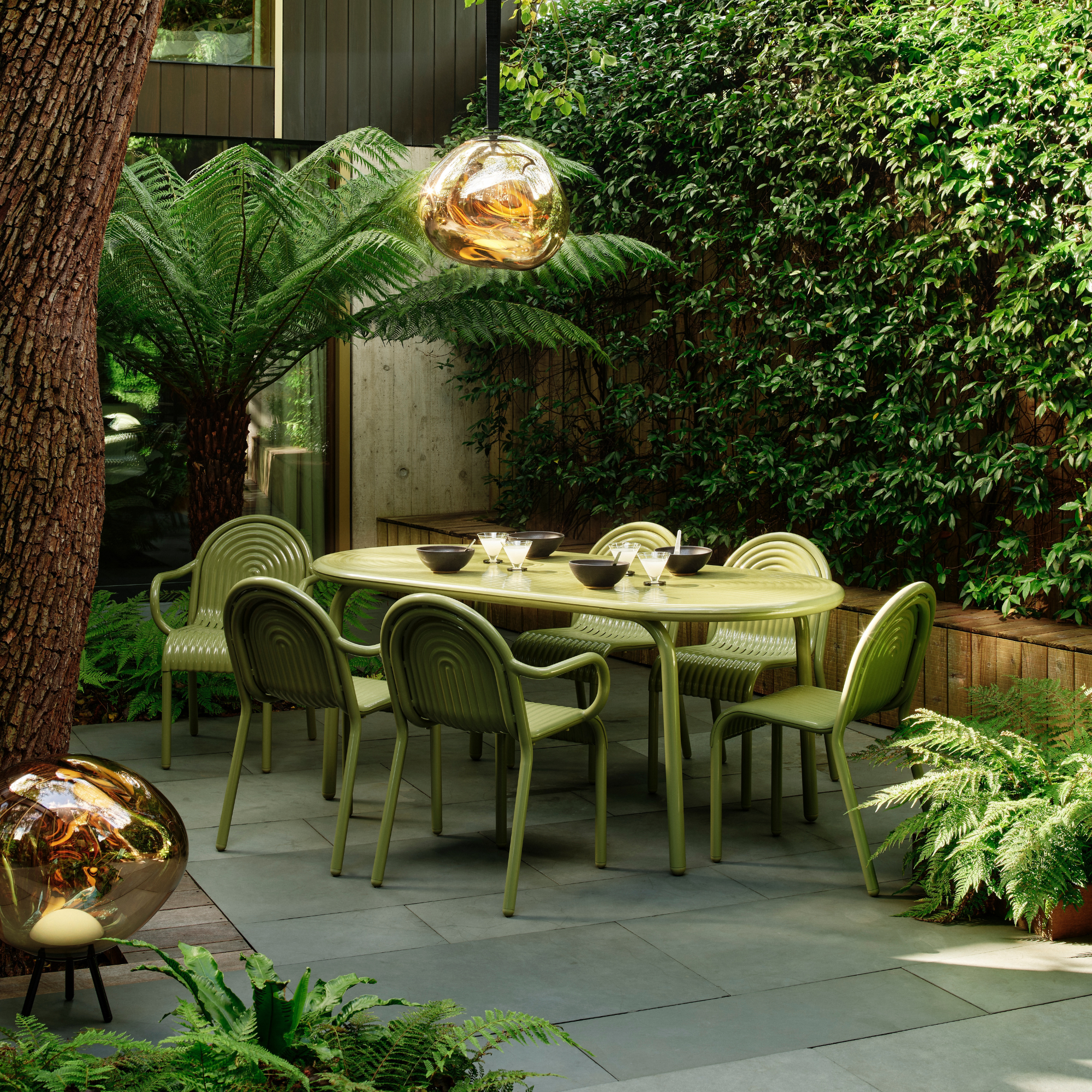 green tom dixon garden furniture on patio surrounded by green hedge