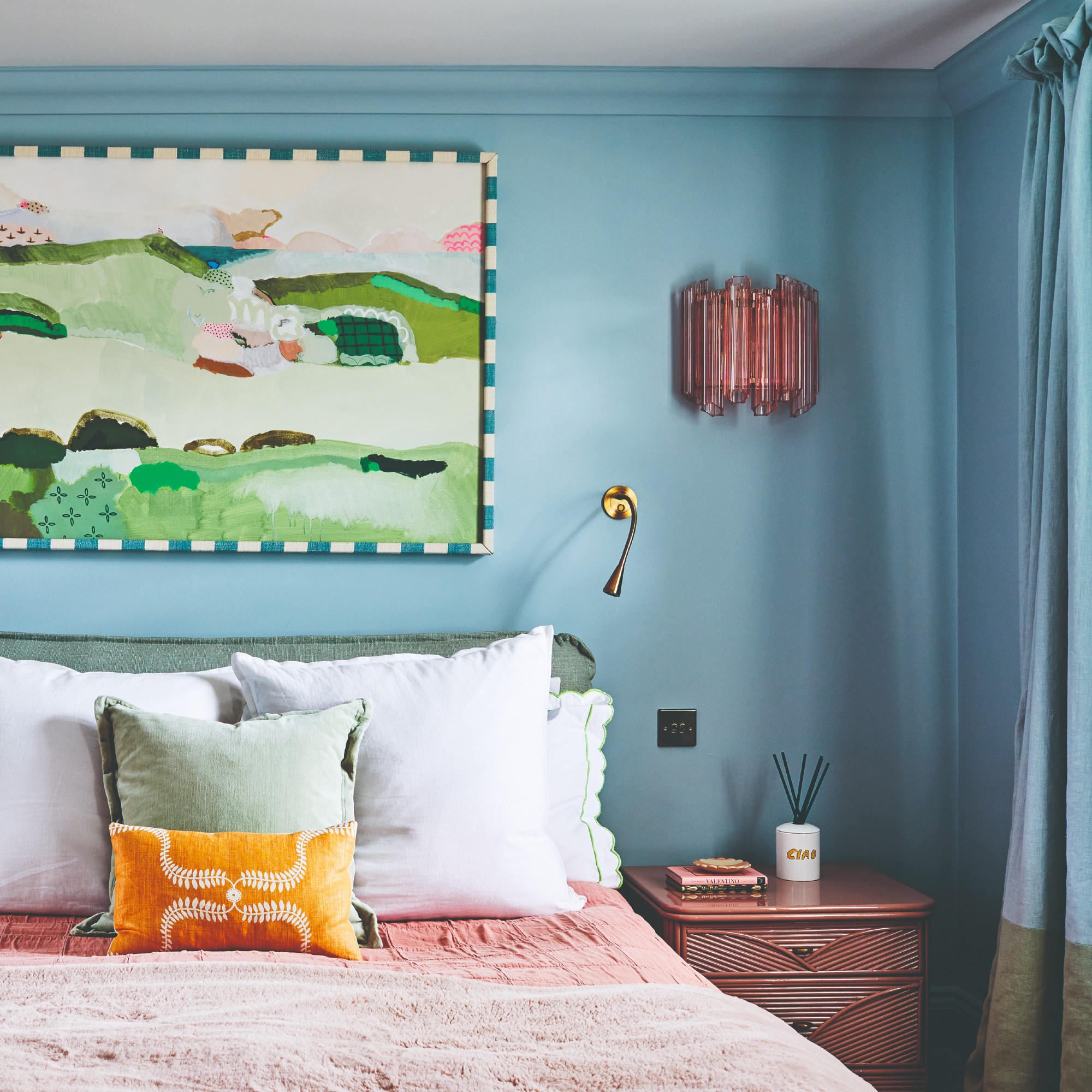 A blue-painted bedroom with a blue curtain with a green trim and a bright landscape painting on the wall