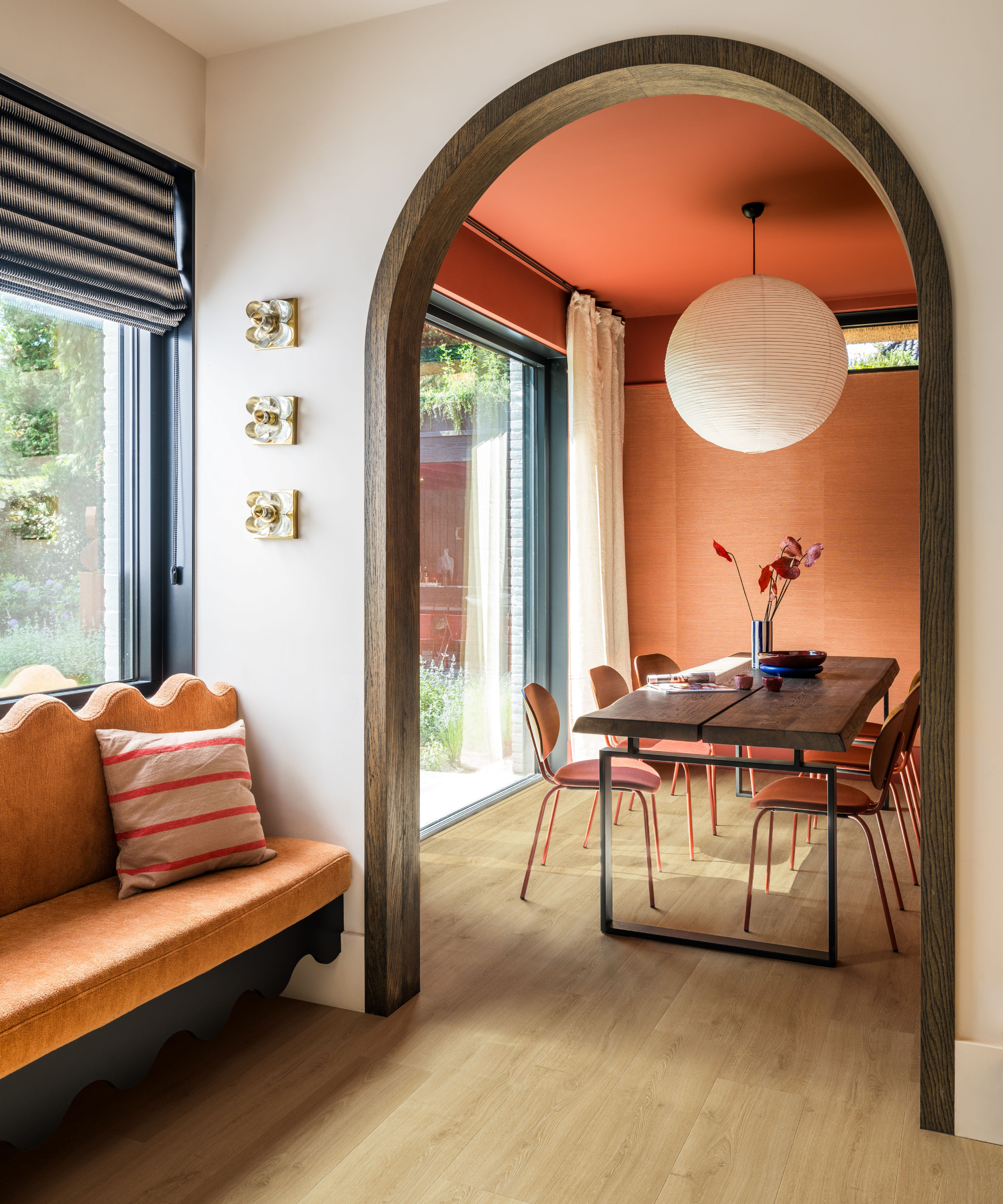 archway leading to dining room with wooden floor, black dining table, orange chairs, orange painted walls, pendant light