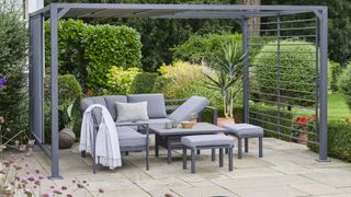dark grey aluminium pergola over grey outdoor sofas, stools and table on patio