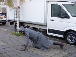 Man on street doing press up in grey puffer jacket with white van behind